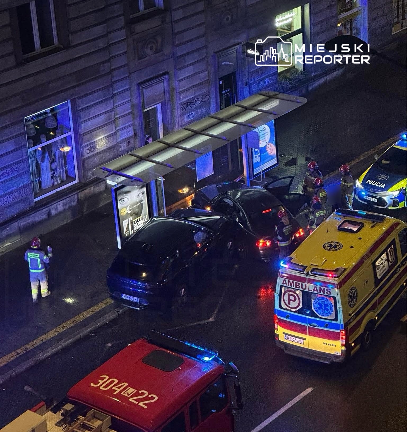 Grupa ratowników i policjantów udziela pomocy po kolizji dwóch samochodów na oświetlonej ulicy.