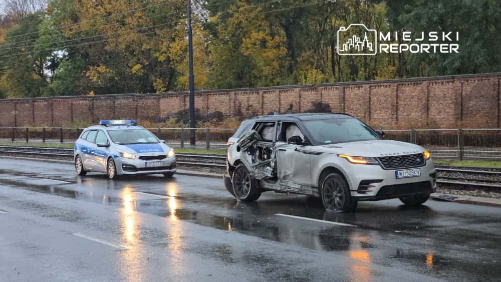 Uszkodzony samochód z otwartymi drzwiami stoi na mokrej jezdni obok radiowozu policyjnego.