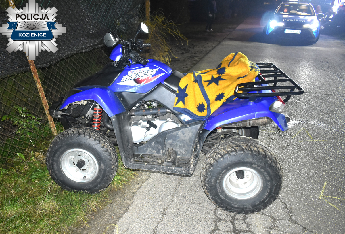 Niebieski quad zaparkowany na poboczu drogi, przykryty żółtym kocem w gwiazdy, obok policyjny radiowóz.