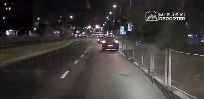 Samochód osobowy porusza się nocą po oświetlonej ulicy, mijając inne pojazdy.