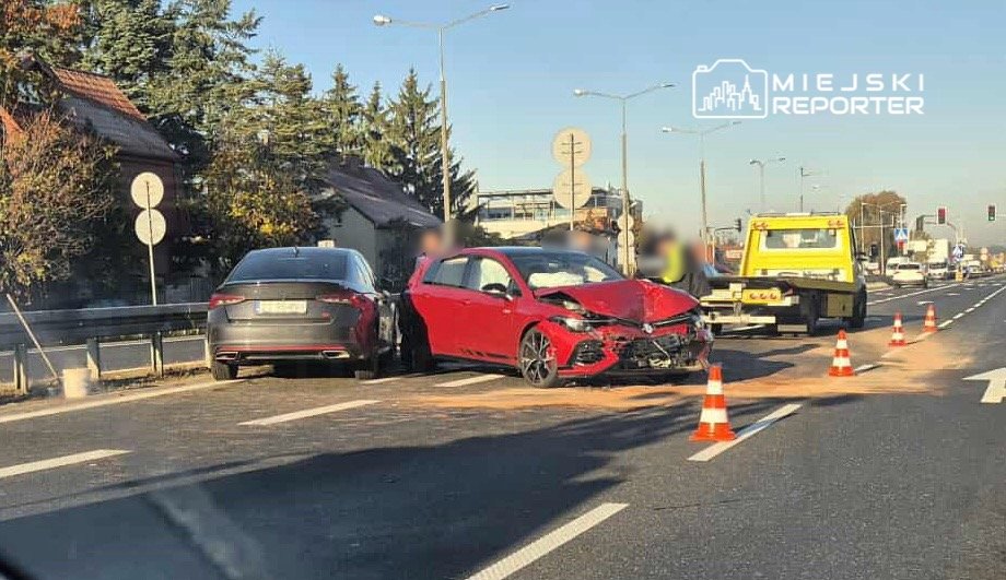 Czerwony samochód osobowy z uszkodzoną przednią częścią stoi na jezdni, obok niego szary pojazd, a w tle holownik.