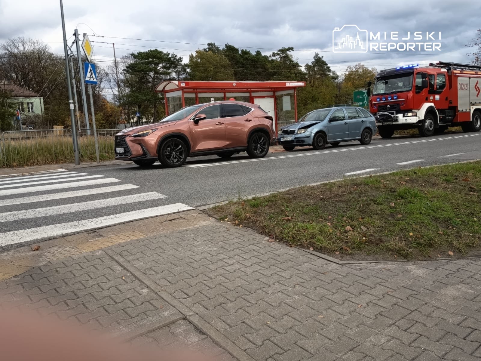 Luksusowy samochód osobowy w kolorze różowym zatrzymany przy przejściu dla pieszych obok niebieskiego auta i wozu strażackiego.