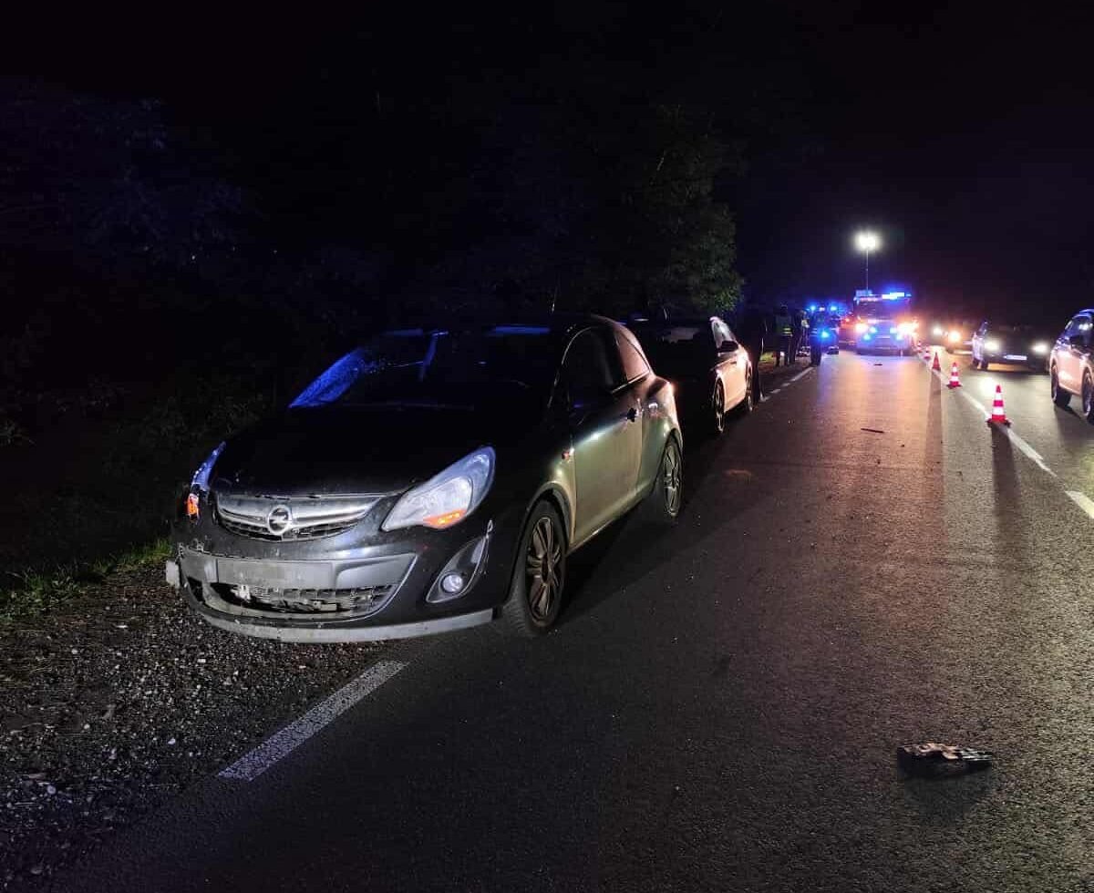 Uszkodzony samochód zaparkowany na poboczu drogi, w tle widać policyjne pojazdy i trójkąty ostrzegawcze.