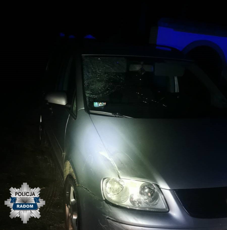 Uszkodzony samochód osobowy z pękniętą szybą przednią, zaparkowany w ciemnym otoczeniu z niebieskim oświetleniem.