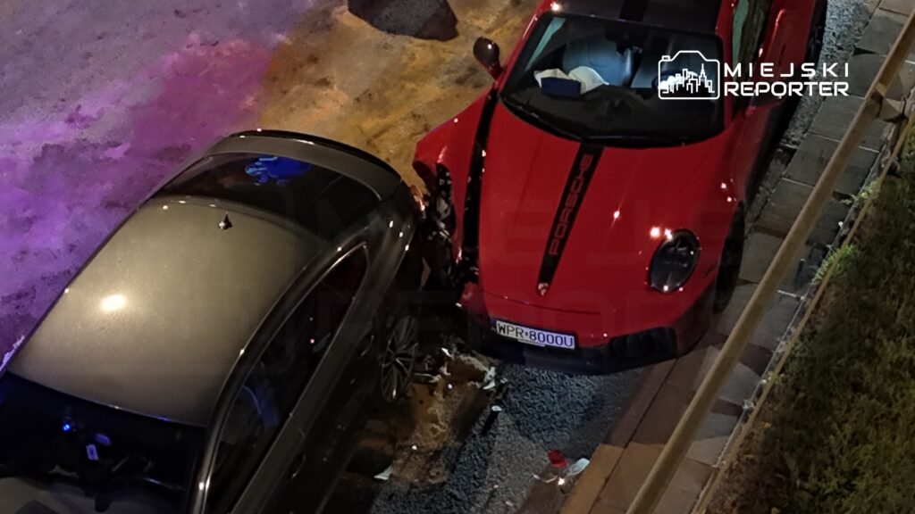 Zderzenie dwóch samochodów na ulicy, czerwony Porsche uszkodzone z boku przez czarny pojazd.