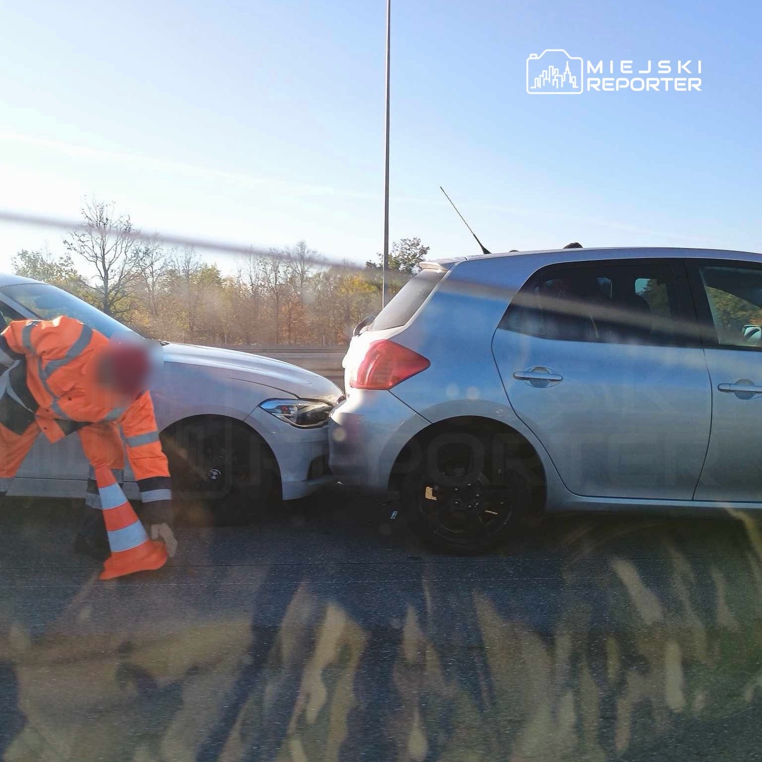 Osoba w pomarańczowym uniformie sprawdza uszkodzenia dwóch zderzających się samochodów na drodze.