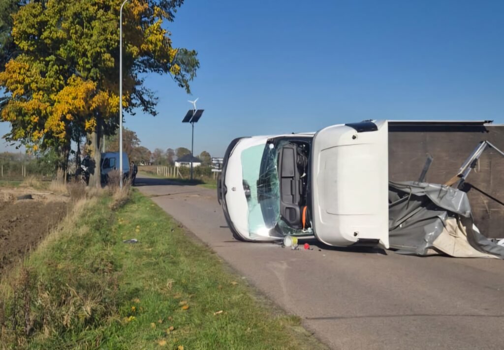 Przewrócony samochód dostawczy leży na boku na drodze, w otoczeniu drzew i pól.