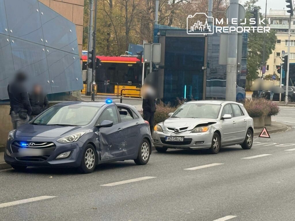 Dwa uszkodzone samochody osobowe stoją na drodze, obok ich kierowców rozmawiają mężczyźni.
