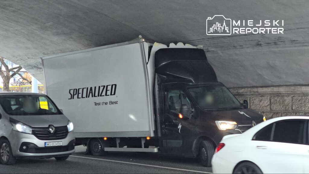 Wysoka ciężarówka z logo "SPECIALIZED" utknęła pod niskim wiaduktem, blokując ruch na jezdni.