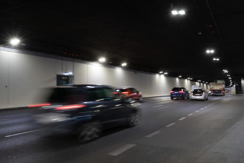Samochody poruszające się z dużą prędkością w oświetlonym tunelu drogowym.